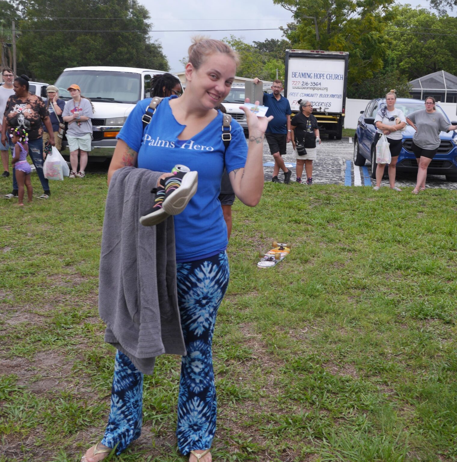 Smiling woman waving, holding towel and shoes
